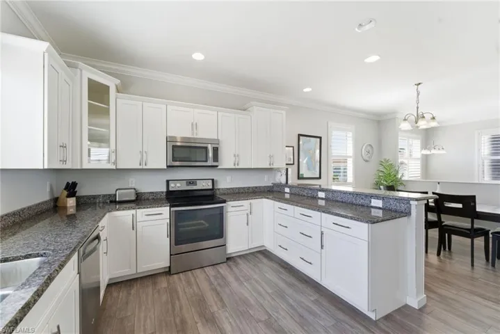 Kitchen with appliances with stainless steel finishes, ornamental molding, hanging light fixtures, white cabinetry, and a peninsula