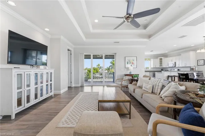 Living room with ornamental molding, recessed lighting, wood finished floors, a raised ceiling, and ceiling fan