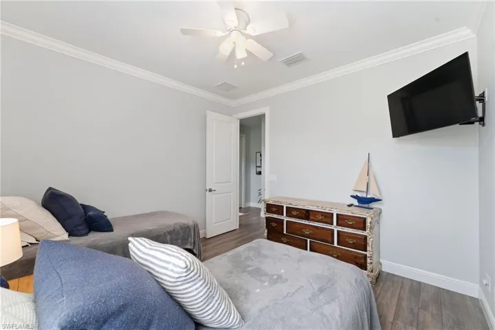 Bedroom with ornamental molding, dark wood-type flooring, and a ceiling fan