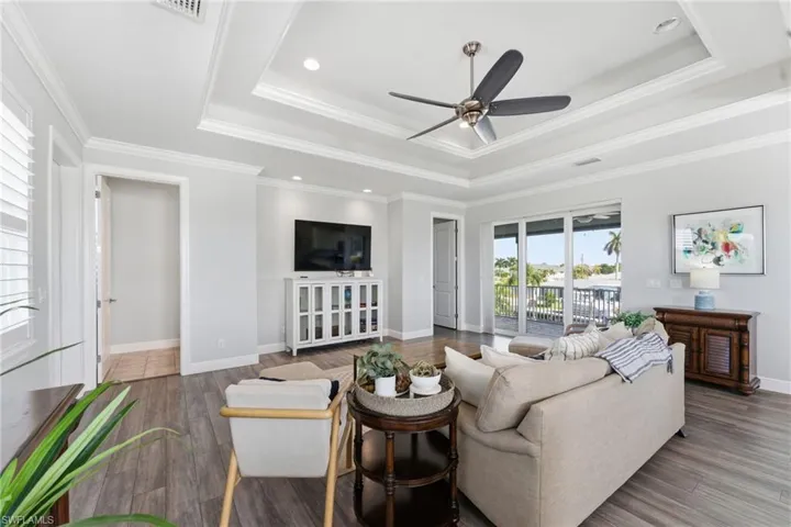 Living room featuring a tray ceiling, ornamental molding, wood finished floors, a ceiling fan, and recessed lighting