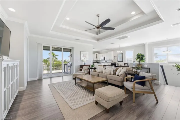 Living room with a chandelier, a raised ceiling, crown molding, ceiling fan, and plenty of natural light