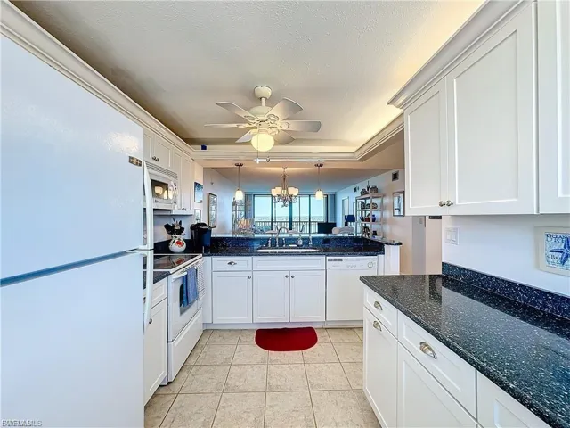 Kitchen with white appliances, hanging light fixtures, white cabinets, dark stone countertops, and light tile patterned floors