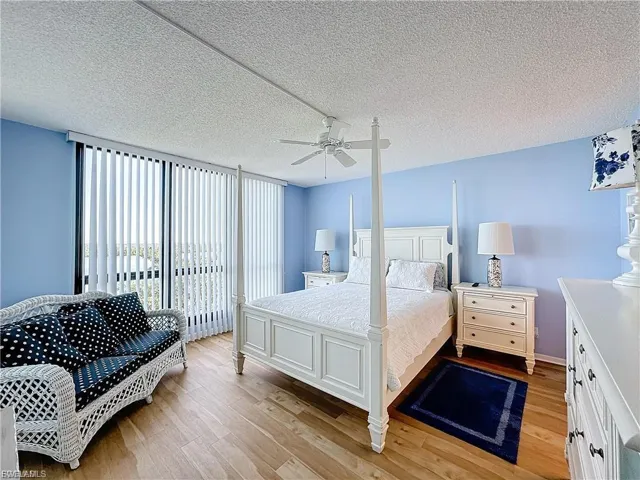 Bedroom with a textured ceiling, light wood-style flooring, expansive windows, ceiling fan, and access to exterior