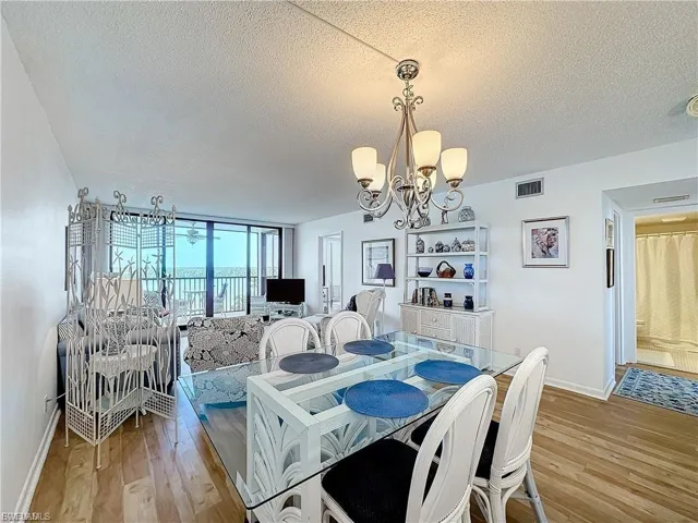 Dining space featuring a chandelier, a textured ceiling, light wood-type flooring, and a wall of windows