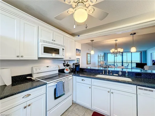 Kitchen featuring white appliances, a chandelier, decorative light fixtures, white cabinetry, and light tile patterned floors