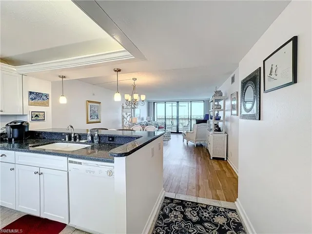 Kitchen with white cabinets, dishwasher, a chandelier, decorative light fixtures, and dark stone countertops