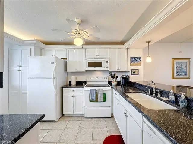 Kitchen featuring white appliances, white cabinets, dark stone counters, pendant lighting, and light tile patterned flooring