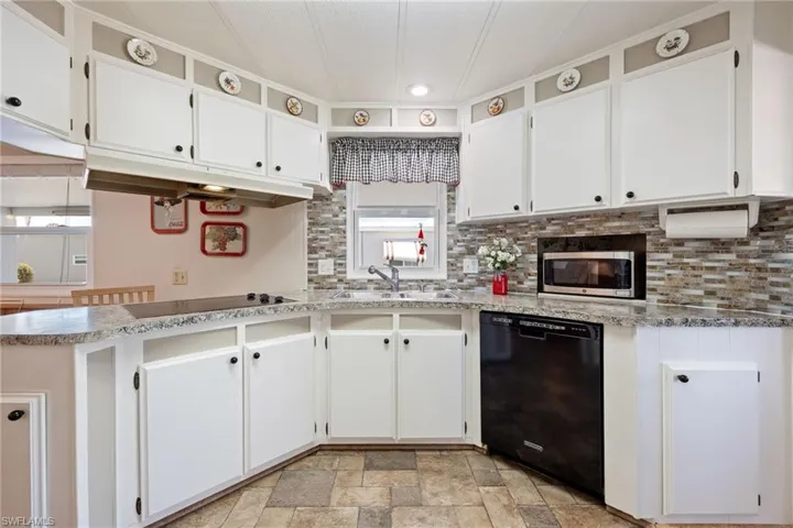 Kitchen with black appliances, white cabinets, stone finish floors, and decorative backsplash