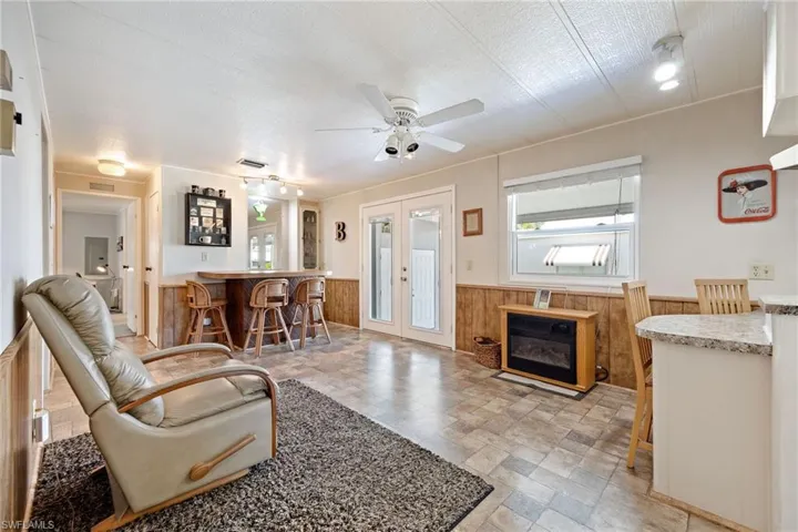 Living area featuring stone finish flooring, wooden walls, wainscoting, a bar, and french doors