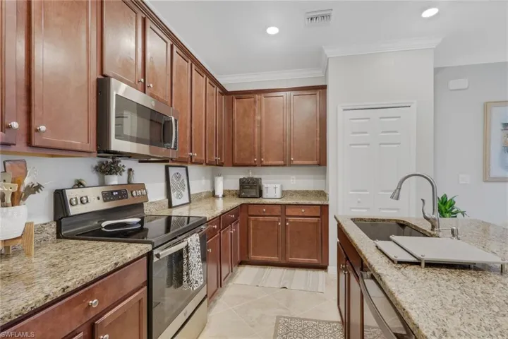 Kitchen with stainless steel appliances, light stone countertops, light tile patterned floors, crown molding, and recessed lighting