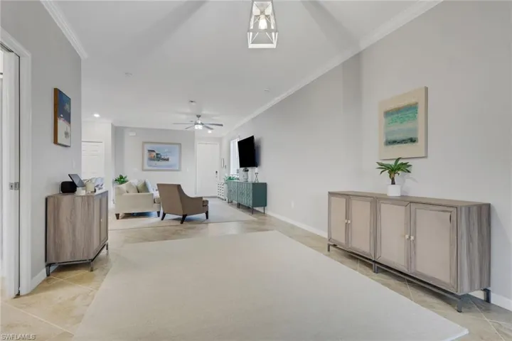Living room with crown molding, light tile patterned flooring, and a ceiling fan