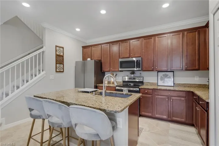 Kitchen featuring stainless steel appliances, a kitchen bar, light stone countertops, an island with sink, and light tile patterned floors