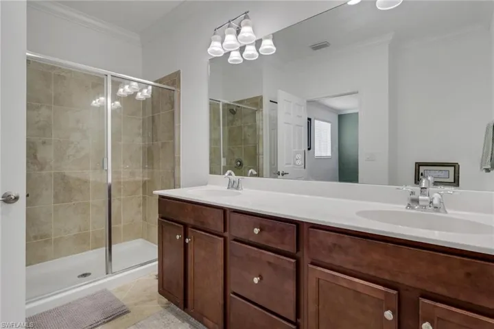 Bathroom with double vanity, a shower stall, crown molding, and light tile patterned floors
