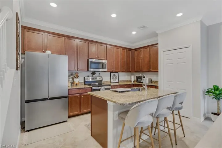 Kitchen featuring stainless steel appliances, light stone counters, a kitchen breakfast bar, ornamental molding, and recessed lighting