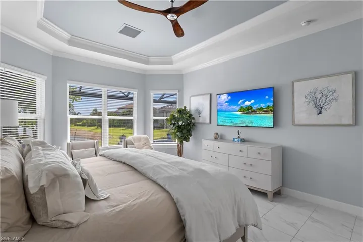 Bedroom with a raised ceiling, light marble finish flooring, ornamental molding, and ceiling fan