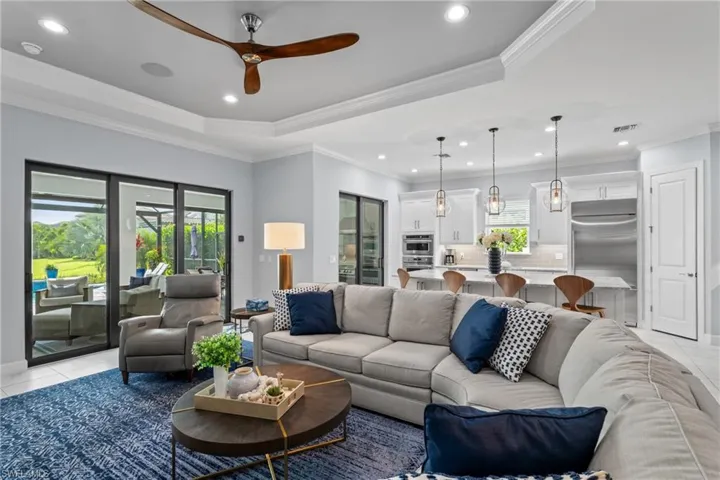 Living room featuring a ceiling fan, recessed lighting, a tray ceiling, light tile patterned flooring, and ornamental molding