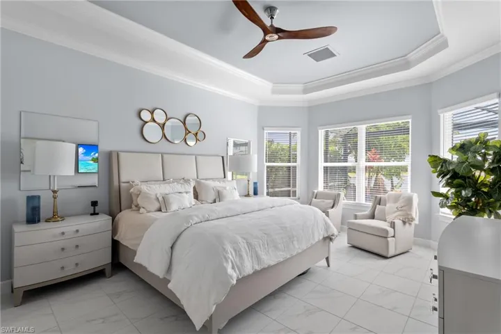 Bedroom featuring light marble finish floors, a tray ceiling, crown molding, and ceiling fan