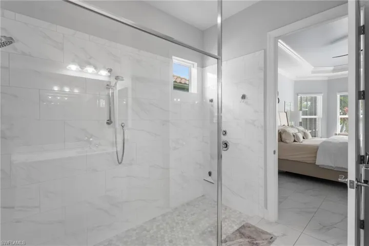 Ensuite bathroom with ornamental molding, a marble finish shower, marble finish floors, and a raised ceiling