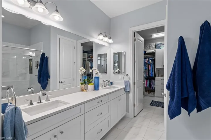 Full bath featuring double vanity, a walk in closet, a stall shower, and marble look tile flooring