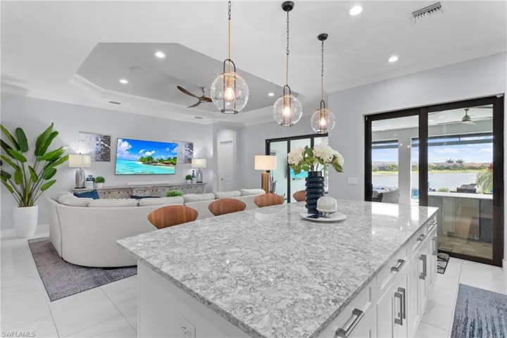 Kitchen featuring a ceiling fan, ornamental molding, white cabinetry, light stone counters, and pendant lighting