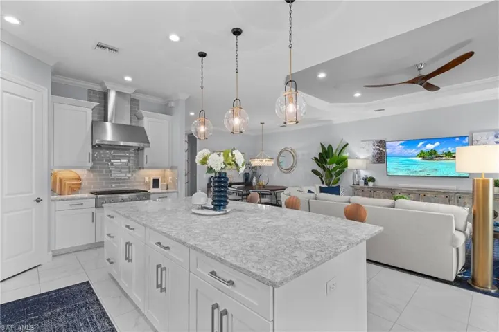 Kitchen with wall chimney exhaust hood, ornamental molding, light marble finish floors, a center island, and decorative backsplash