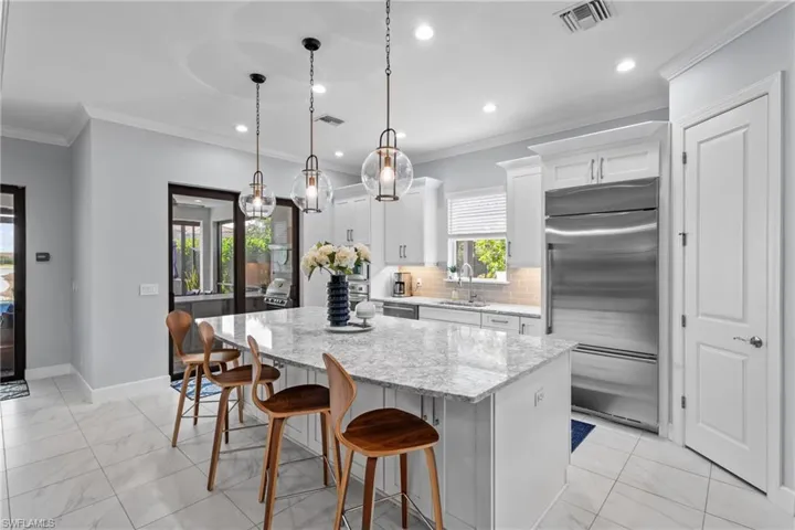 Kitchen with appliances with stainless steel finishes, light marble finish floors, a kitchen island, crown molding, and a kitchen bar