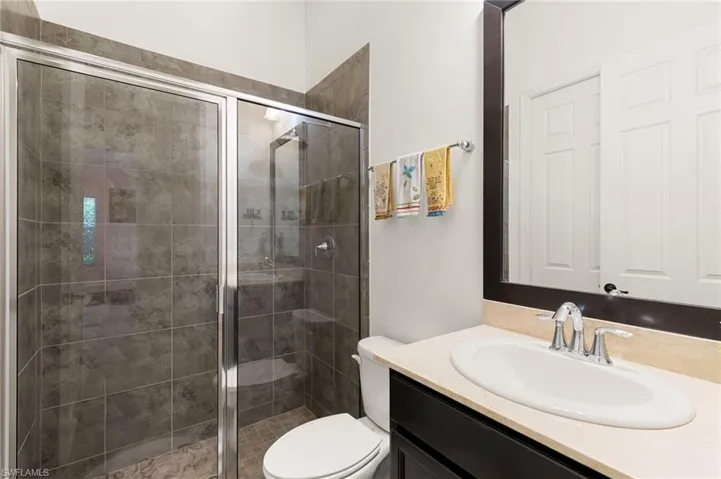First Floor Bathroom #2 featuring a glass-enclosed shower with full tile surround, vanity with an integrated sink and light-toned countertop, dark wood-finish framed mirror, and chrome fixtures