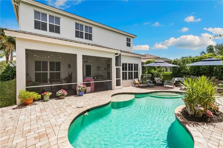 Backyard oasis featuring a curvilinear pool with integrated spa, paver patio, screened lanai, and lush landscaping