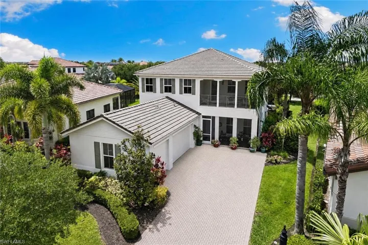 White stucco exterior with a tiled roof, screened balconies, a two-car garage, and a paver driveway