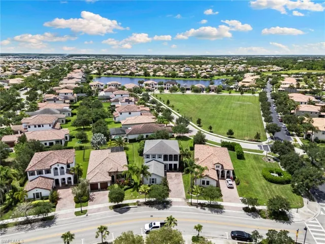 Aerial perspective showcasing a residential community with numerous single-family homes, a large central green space, and a prominent lake