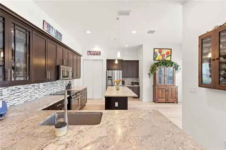 Kitchen featuring extensive counter space, an undermount stainless steel sink, dark wood cabinetry, a tile backsplash, and light wood-finish flooring