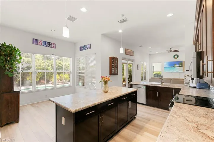 Expansive kitchen featuring a central island with a light-colored countertop, dark wood cabinetry, recessed lighting, and wood-finish flooring