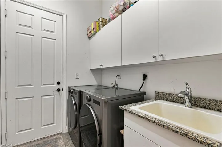 Utility room featuring a built-in sink with a speckled countertop, white cabinetry for storage, and a paneled door