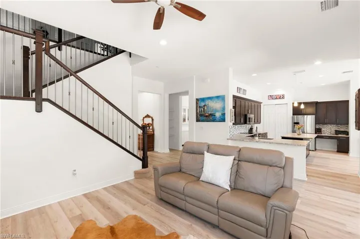 Open-concept living area featuring wood-finish flooring, a contemporary staircase with dark wood railings and metal balusters, recessed lighting, and a ceiling fan