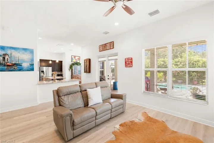 Open-concept living area featuring light wood-finish flooring, a contemporary ceiling fan, and large windows with horizontal blinds