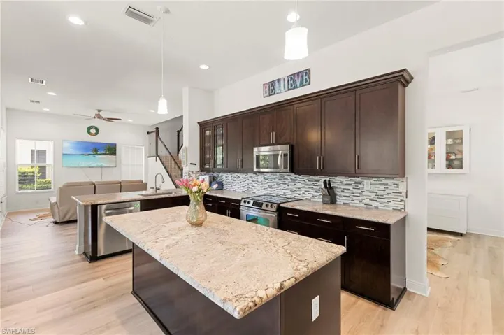 Kitchen featuring an island with granite countertops, dark wood cabinetry, a stainless steel microwave, and a mosaic tile backsplash