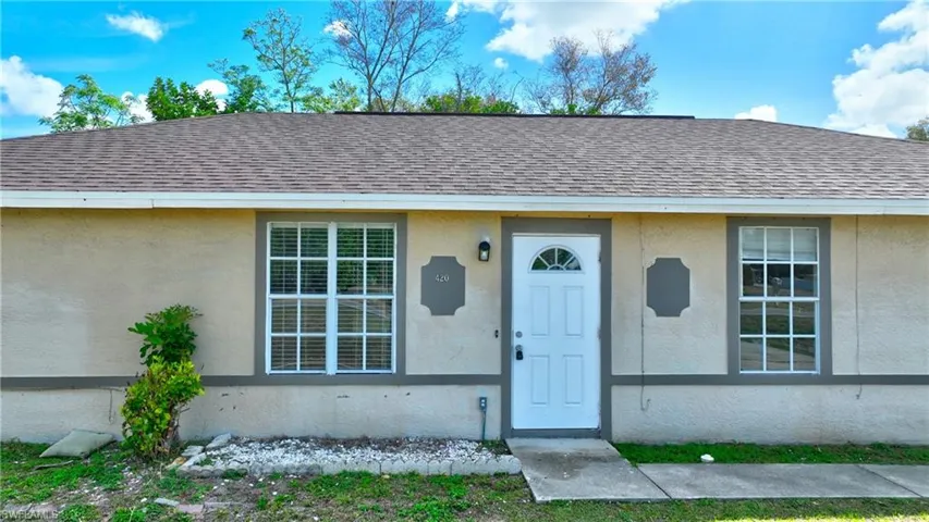 Doorway to property with a shingled roof and stucco siding