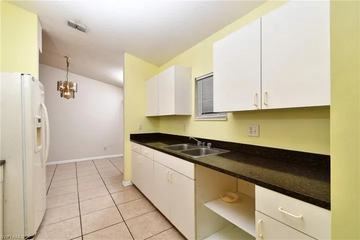 Kitchen with white cabinetry, white fridge with ice dispenser, light tile patterned floors, and suspended lighting