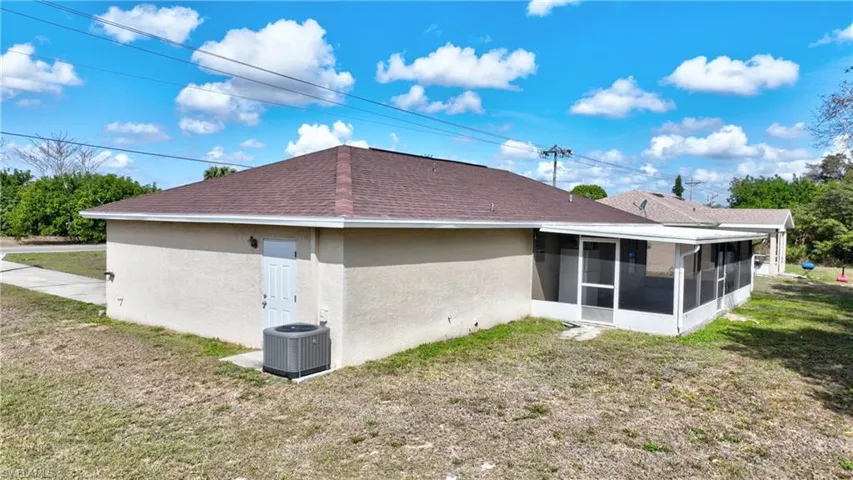 Rear view of property with stucco siding, a yard, roof with shingles, and a sunroom