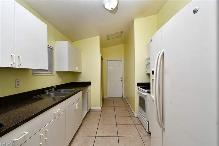Kitchen featuring white appliances, dark countertops, white cabinetry, light tile patterned floors, and vaulted ceiling