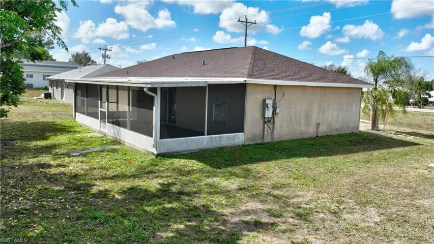 Back of house with a yard, a sunroom, stucco siding, and roof with shingles