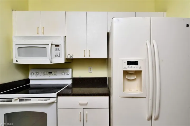 Kitchen featuring white appliances, dark countertops, and white cabinets