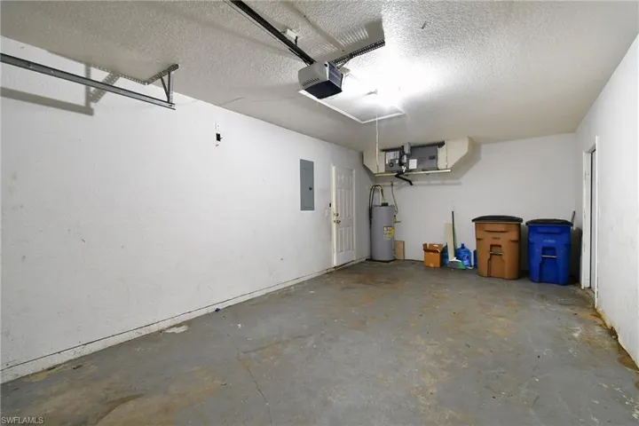 Garage with electric water heater, electric panel, and a garage door opener