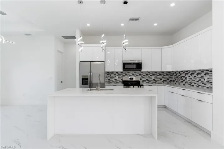 Kitchen featuring modern cabinets, light stone countertops, stainless steel appliances, white cabinetry, and an island with sink