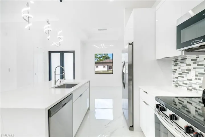 Kitchen featuring modern cabinets, white cabinets, stainless steel appliances, light stone counters, and a kitchen island with sink