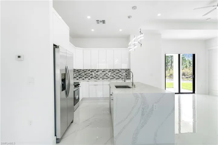 Kitchen with white cabinets, decorative light fixtures, light stone countertops, and stainless steel appliances