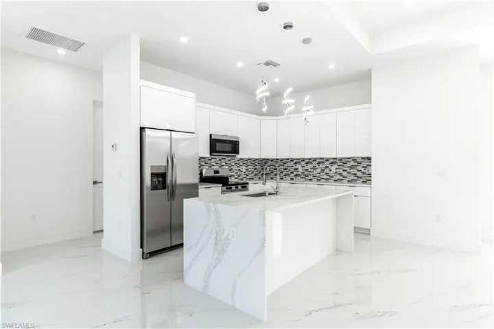 Kitchen with stainless steel appliances, white cabinetry, pendant lighting, modern cabinets, and light stone counters