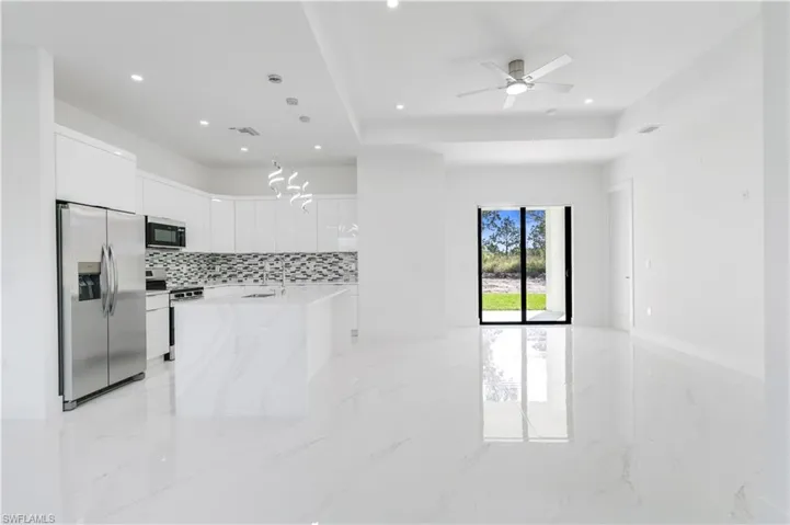 Kitchen featuring stainless steel appliances, light stone counters, white cabinetry, a ceiling fan, and decorative backsplash