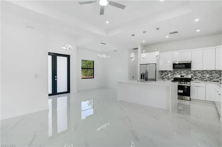 Kitchen with light stone countertops, stainless steel appliances, white cabinetry, a tray ceiling, and a center island with sink