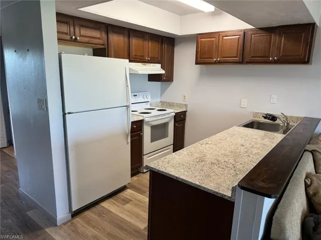 Kitchen with light hardwood / wood-style floors, dark brown cabinetry, sink, white appliances, and a breakfast bar